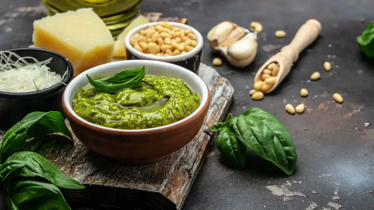 Un cuenco de vibrante pesto de kale, con piñones, ajo, queso Parmesano y hojas de albahaca fresca, listo para realzar cualquier plato.