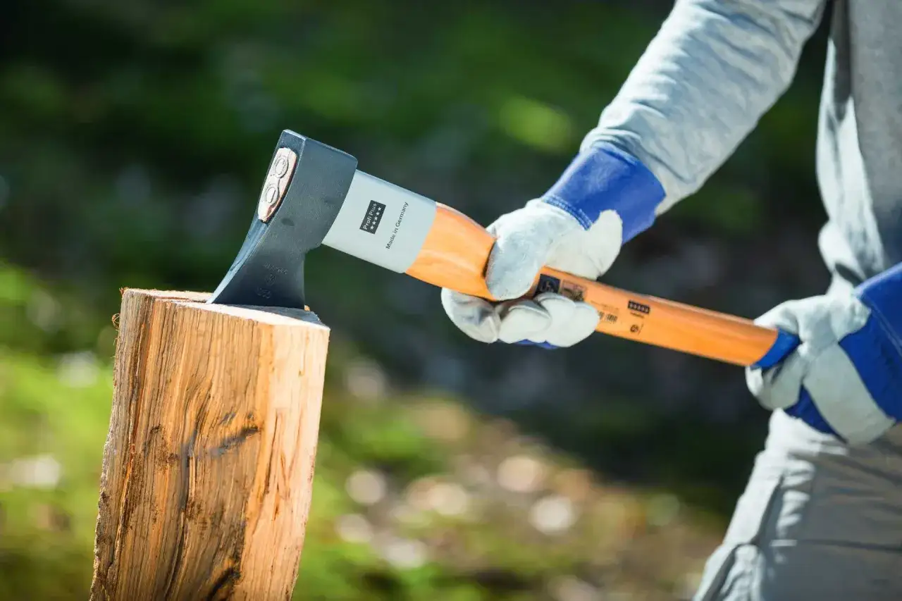 Person mit Handschuhen hält Axt bereit, um Holz zu spalten. Der Spaltprozess beginnt.