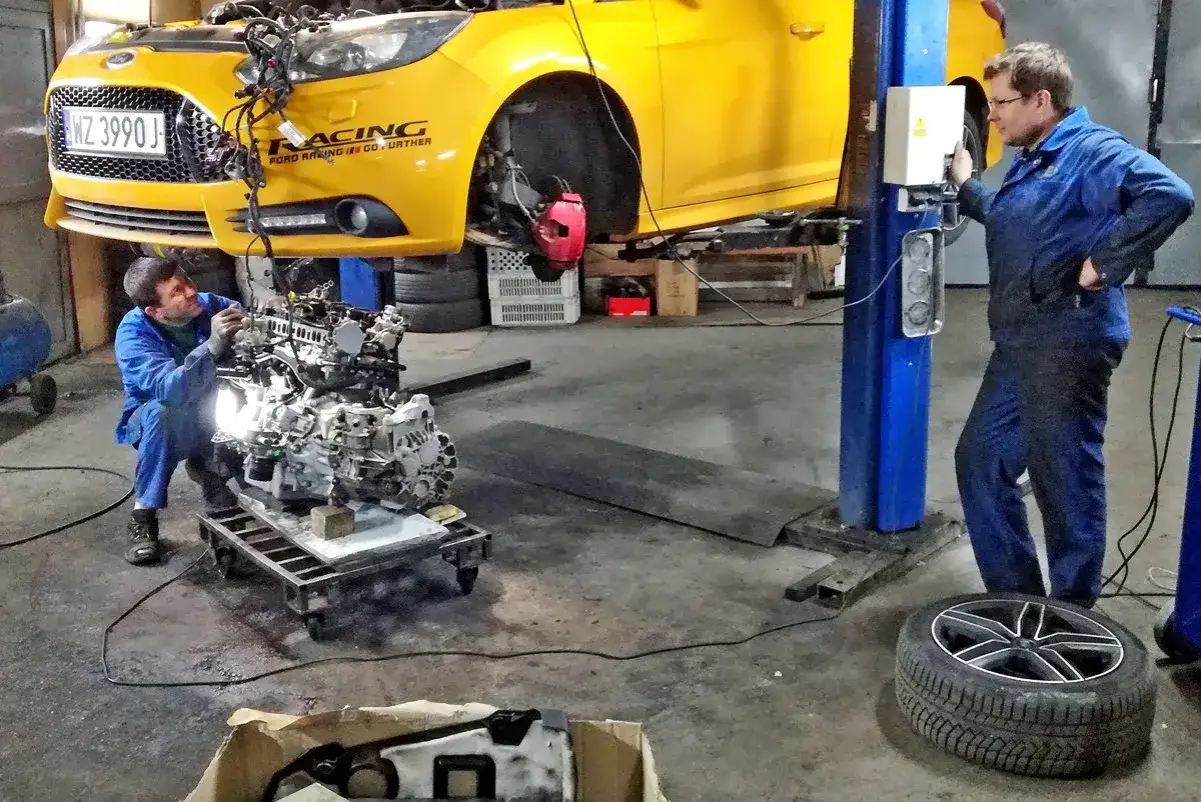 Mechanik pracuje nad wyjętym silnikiem z żółtego Forda. Zastanawiasz się, ile kosztuje wyjęcie silnika z samochodu?