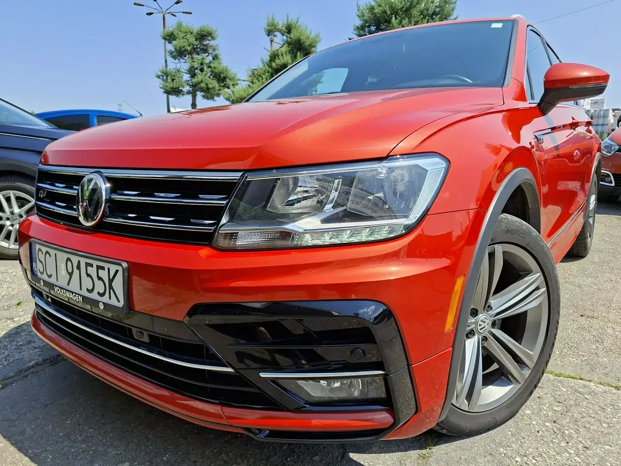 Pomarańczowy Volkswagen Tiguan 5N z czarnymi akcentami i felgami stoi na parkingu.