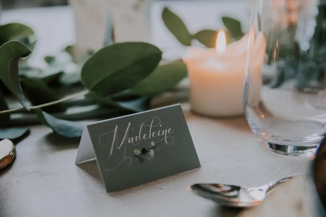 Un porte nom original à faire soi-même, orné d'une calligraphie élégante et d'une touche florale, sur une table dressée avec des bougies et des feuilles vertes.