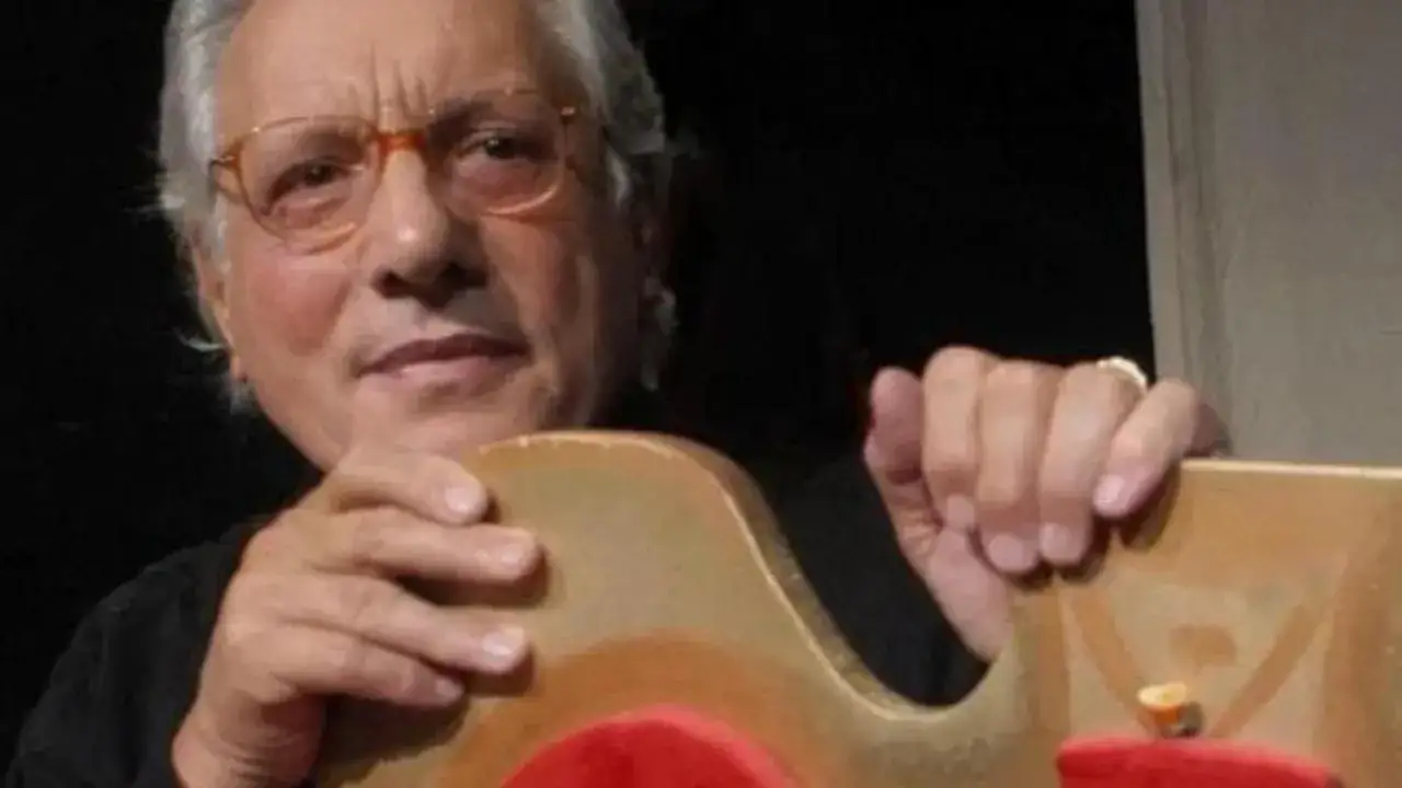 Un uomo con occhiali arancioni tiene un oggetto dorato. Sembra che ho visto un re testo, forse un'opera d'arte.