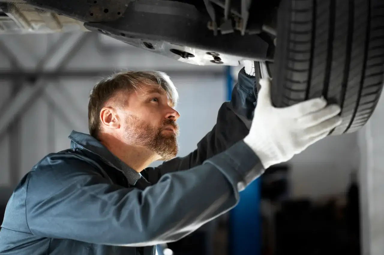 Mechanik w białych rękawiczkach sprawdza oponę, szukając przyczyny głuchego stukania podczas jazdy.