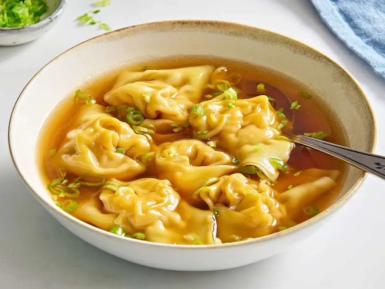 A miseczce paruje aromatyczna zupa wonton, pełna delikatnych pierożków i posypana szczypiorkiem.