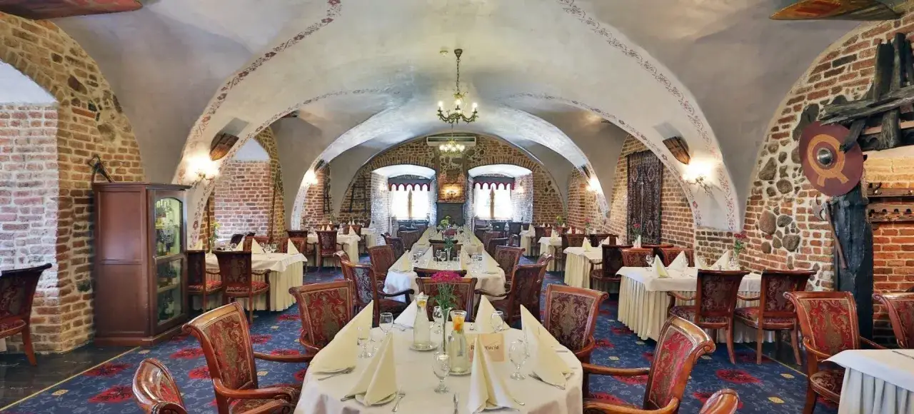 Elegancka restauracja w hotelu zamek, z kamiennymi ścianami, łukowymi sklepieniami i zabytkowymi meblami.
