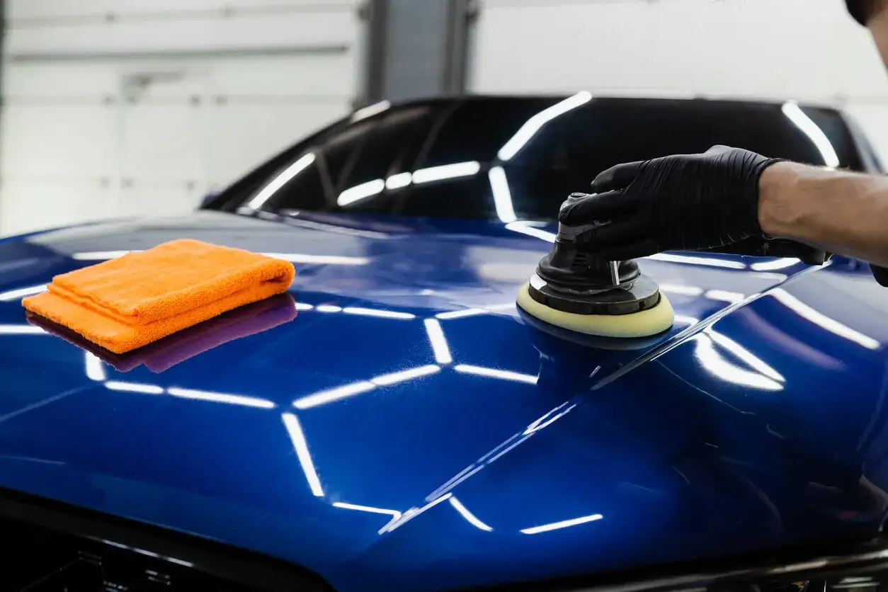Polering av blå bil med polermaskin, en orange trasa ligger bredvid. Ger en glans som en Turtle Wax-finish.