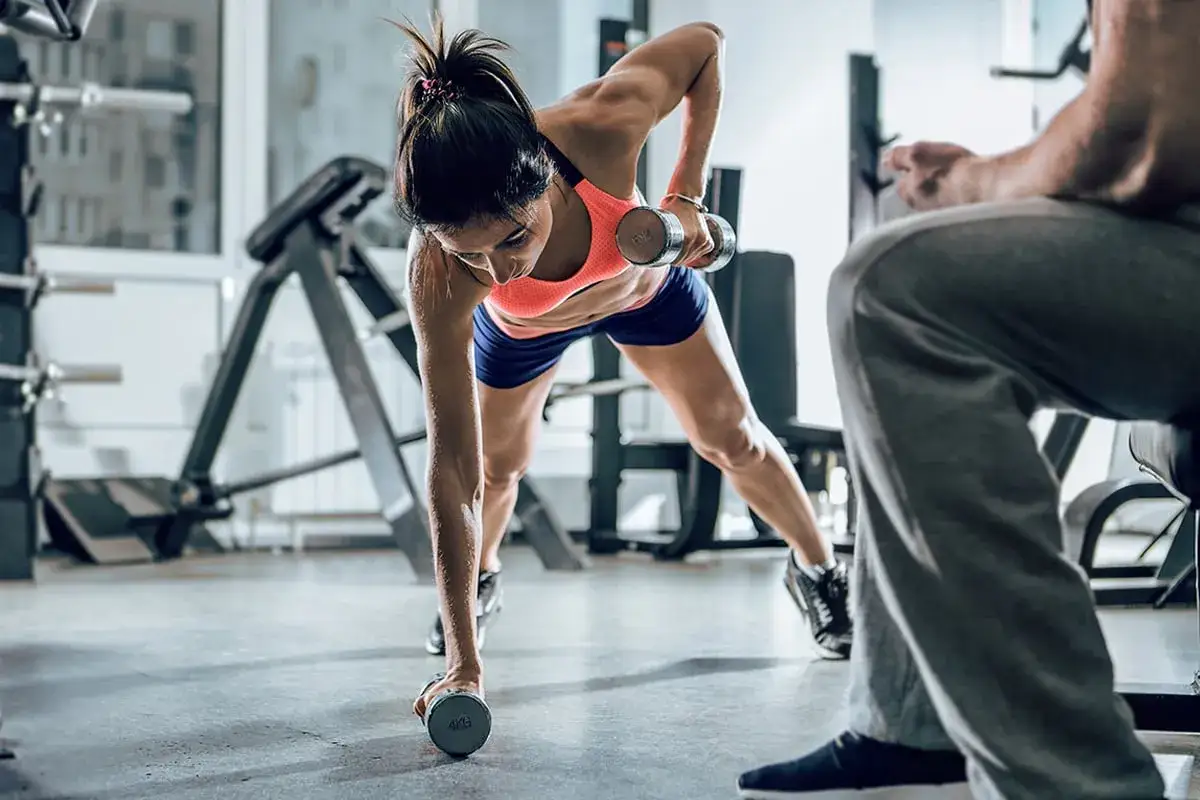 Femme en gainage dynamique, soulevant un haltère. Son corps est gainé, ses muscles tendus, elle se concentre sur son mouvement.