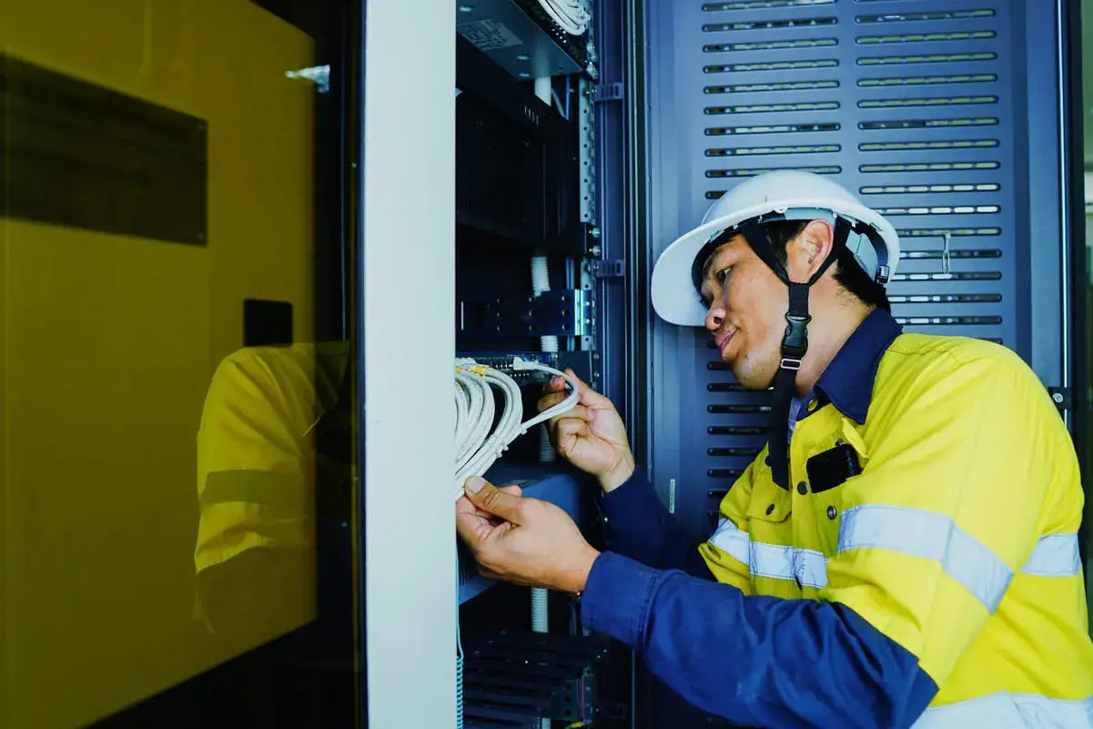 Technicien en fibre optique, casque blanc, gilet jaune, travaillant sur des c&acirc;bles. Installation fibre gratuite en cours.