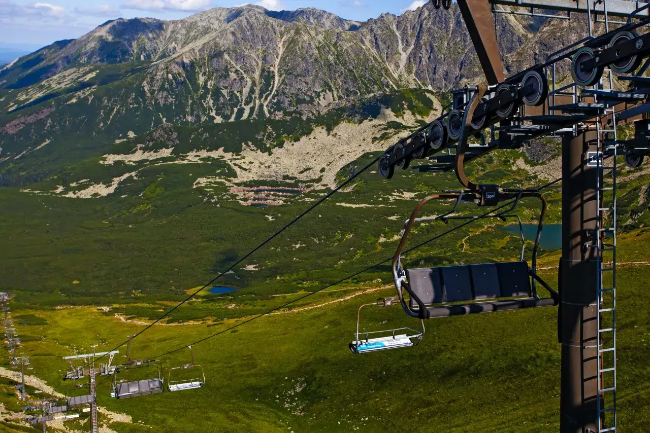 Kolejka linowa na Tatry Kasprowy Wierch. Krzesełka suną nad zielonymi zboczami i skalistymi szczytami.