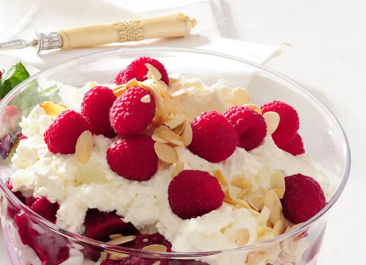Pyszna beza z mascarpone, malinami i płatkami migdał&oacute;w w szklanej misie.
