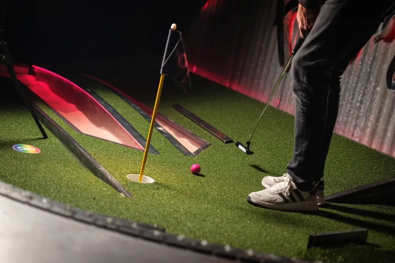 En person spelar minigolf i Slottsskogen. En rosa boll ligger nära hålet, redo för ett slag.