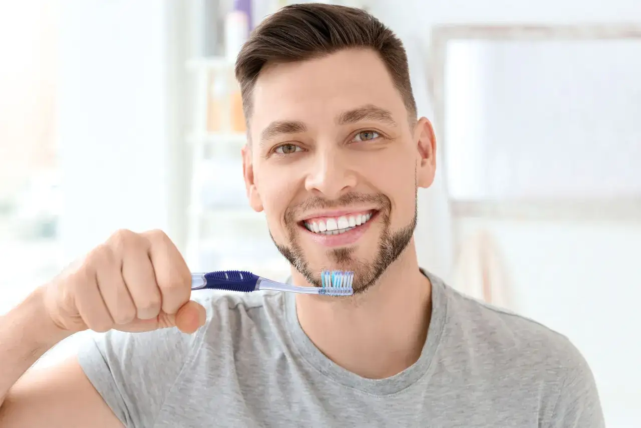Hombre sonriente con cepillo dental, listo para su rutina de higiene bucal.