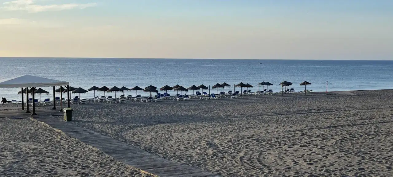 Playa marina de la torre con arena fina, tumbonas y sombrillas alineadas bajo un cielo despejado.