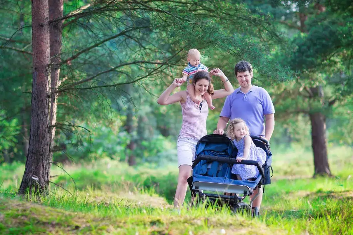 Szczęśliwa rodzina spaceruje po lesie. Mama niesie dziecko na ramionach, a tata pcha wózek z córką. To piękny widok, dla kogo takie becikowe?
