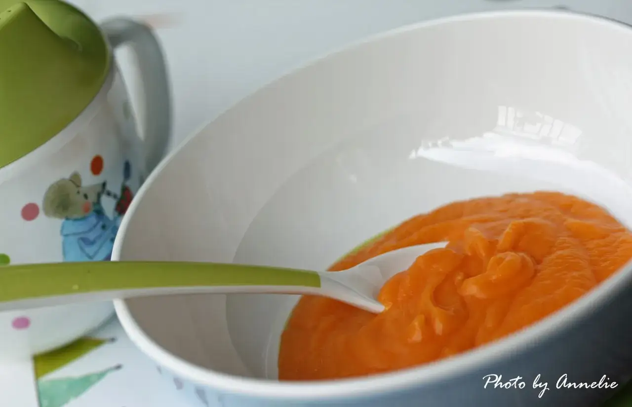 En sk&aring;l med morotspure bebismat, redo att matas. En gr&ouml;n sked ligger i pur&eacute;n.