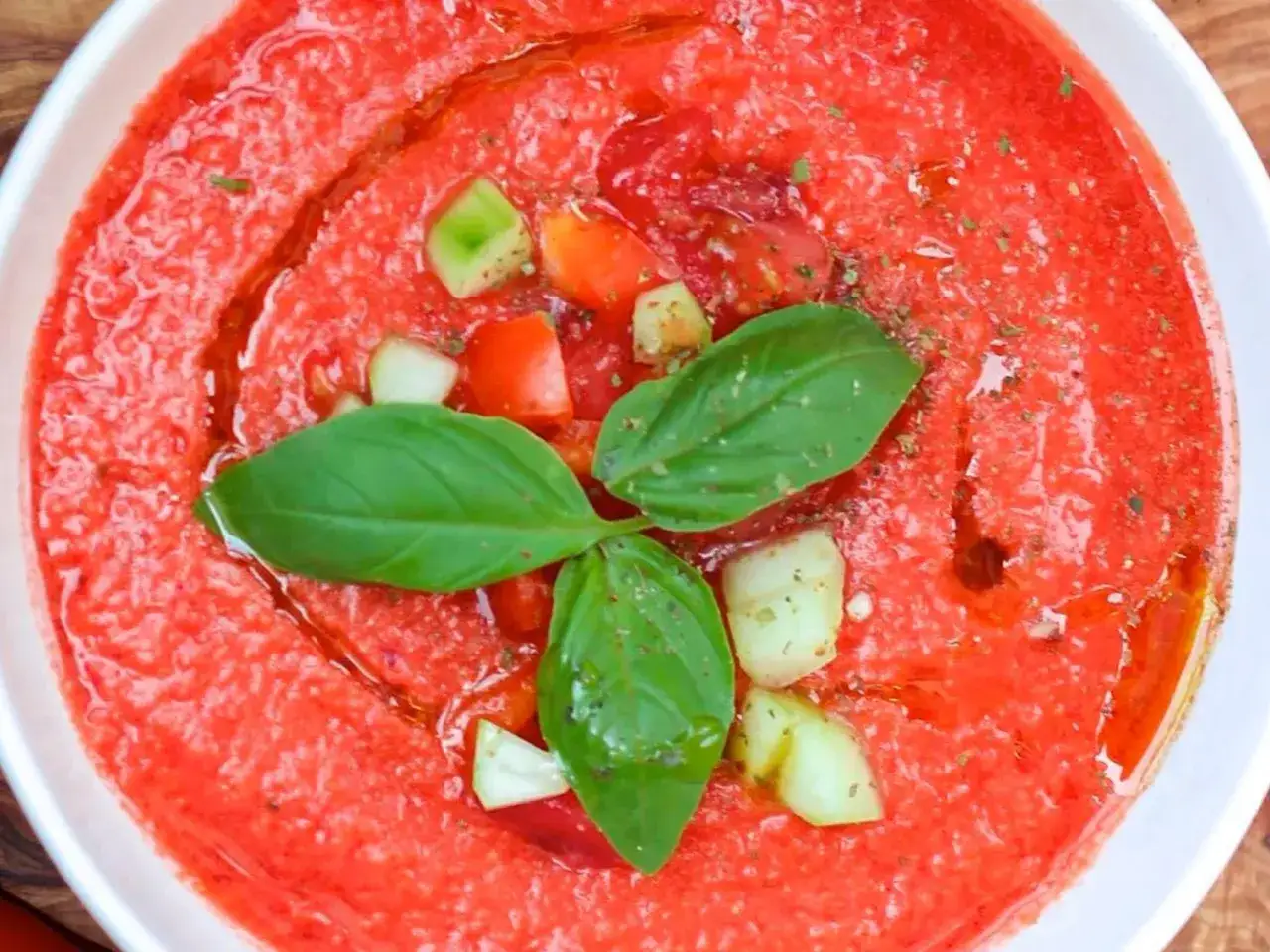 Un bol de sauce tomate maison, garni de d&eacute;s de concombre, de tomates cerises et de feuilles de basilic frais, arros&eacute; d'huile d'olive.