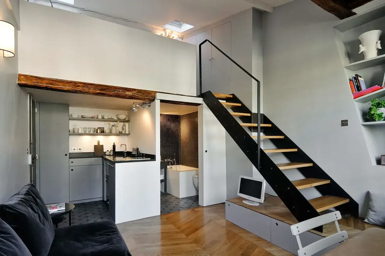 Escalera moderna que aprovecha la **altura del techo** para acceder a un altillo. Cocina compacta y ba&ntilde;o con azulejos.