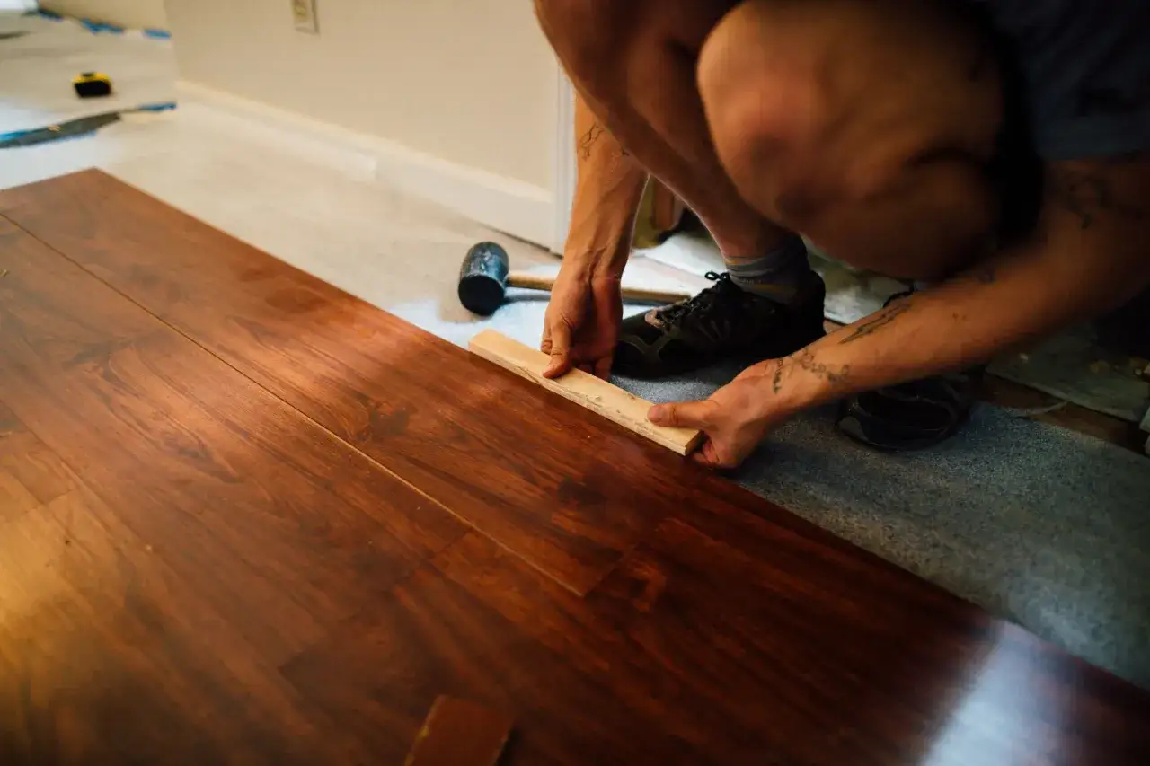 Personen är i färd med att byta golv och lägger ett nytt trägolv.