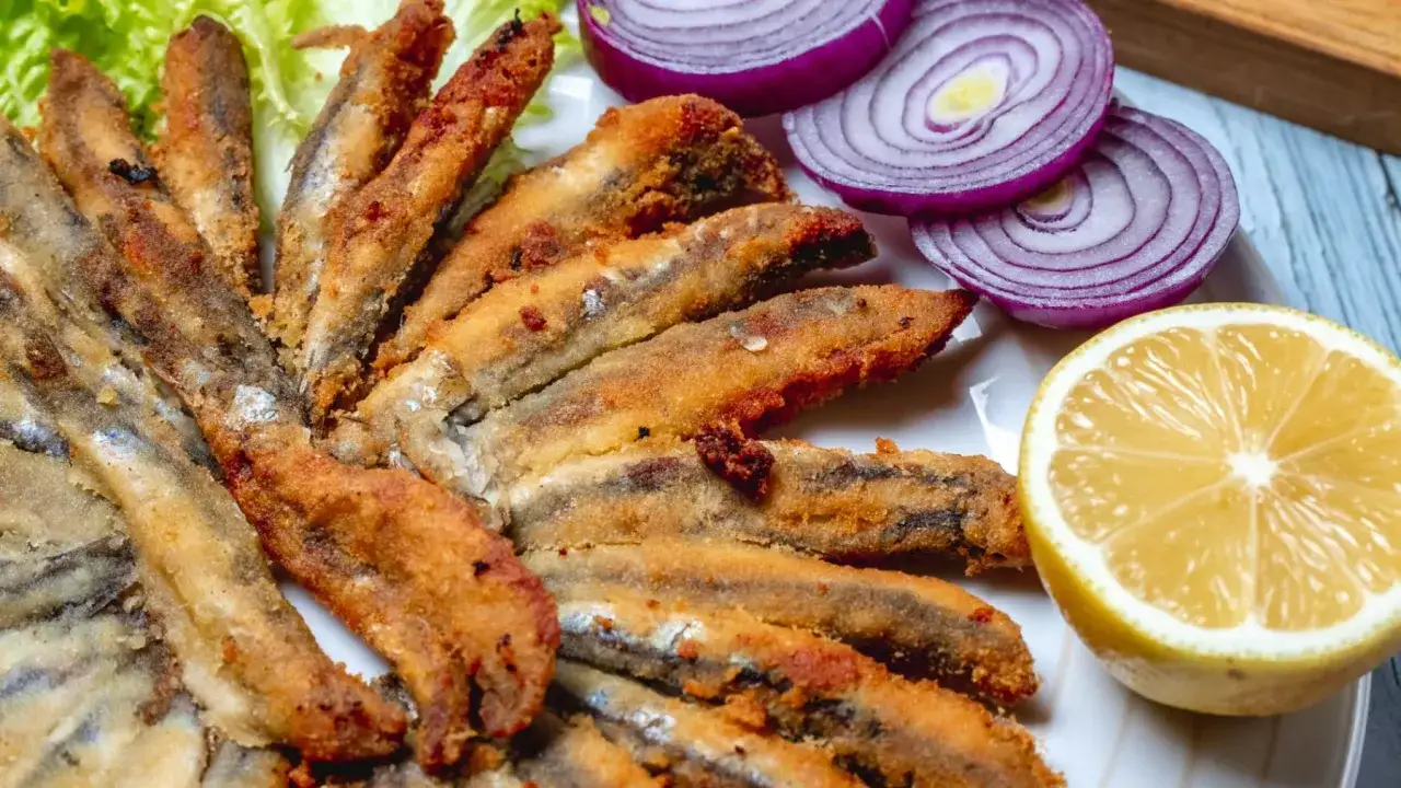 Deliciosa fritura de pescado crujiente, servida con rodajas de cebolla morada y limón fresco.