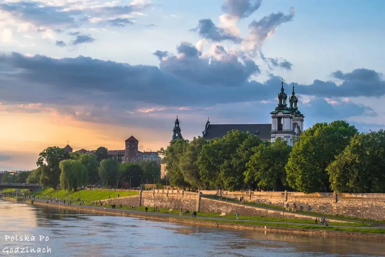 Zach&oacute;d słońca nad Wisłą, ukazujący Wawel i kości&oacute;ł na tle chmur. Piękne miejsca w Krakowie, idealne na spacer.
