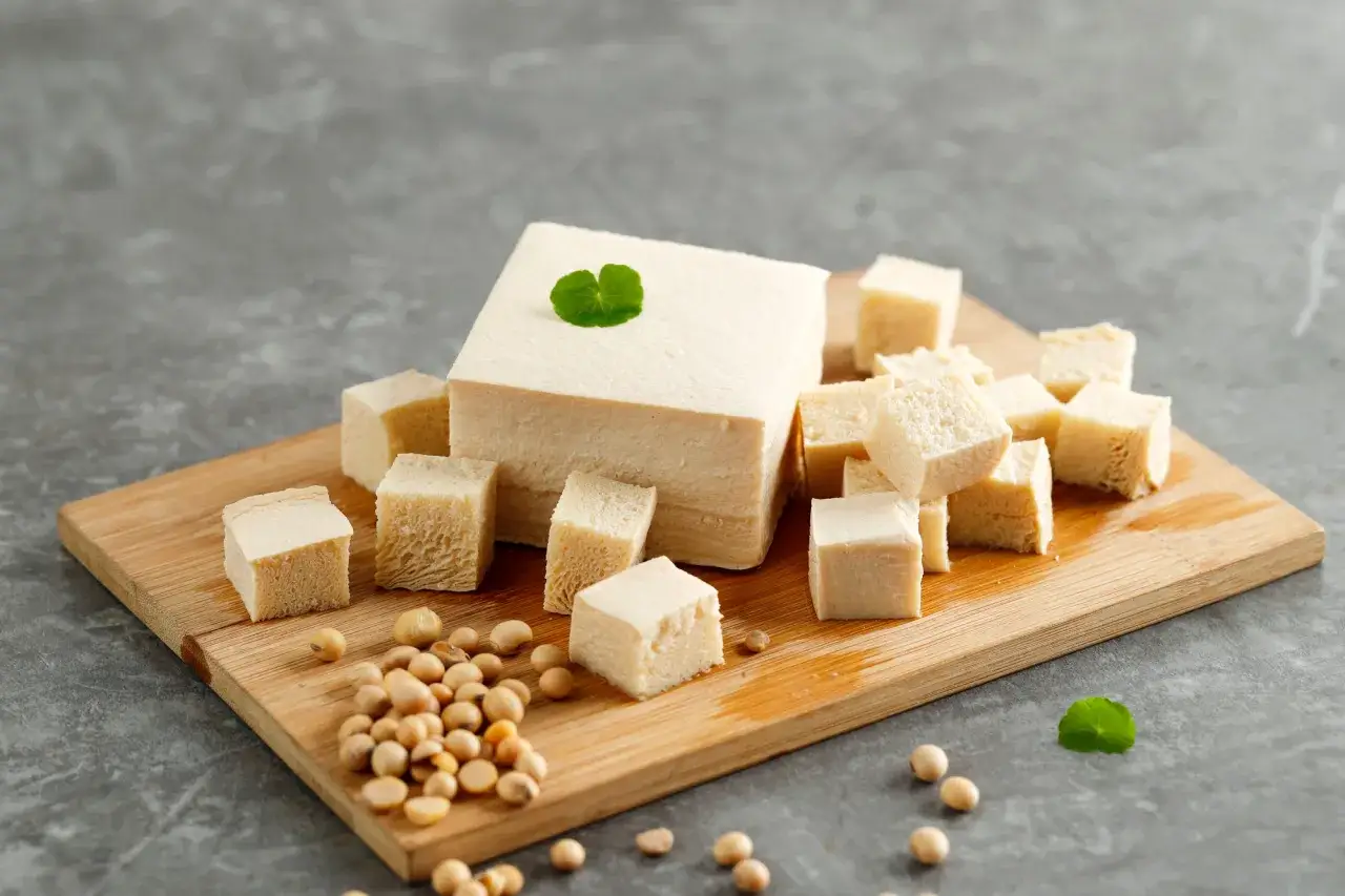 Kostki tofu i ziarna soi na desce. Czy tofu można mrozić? Tak, po rozmrożeniu zachowuje swoje właściwości.