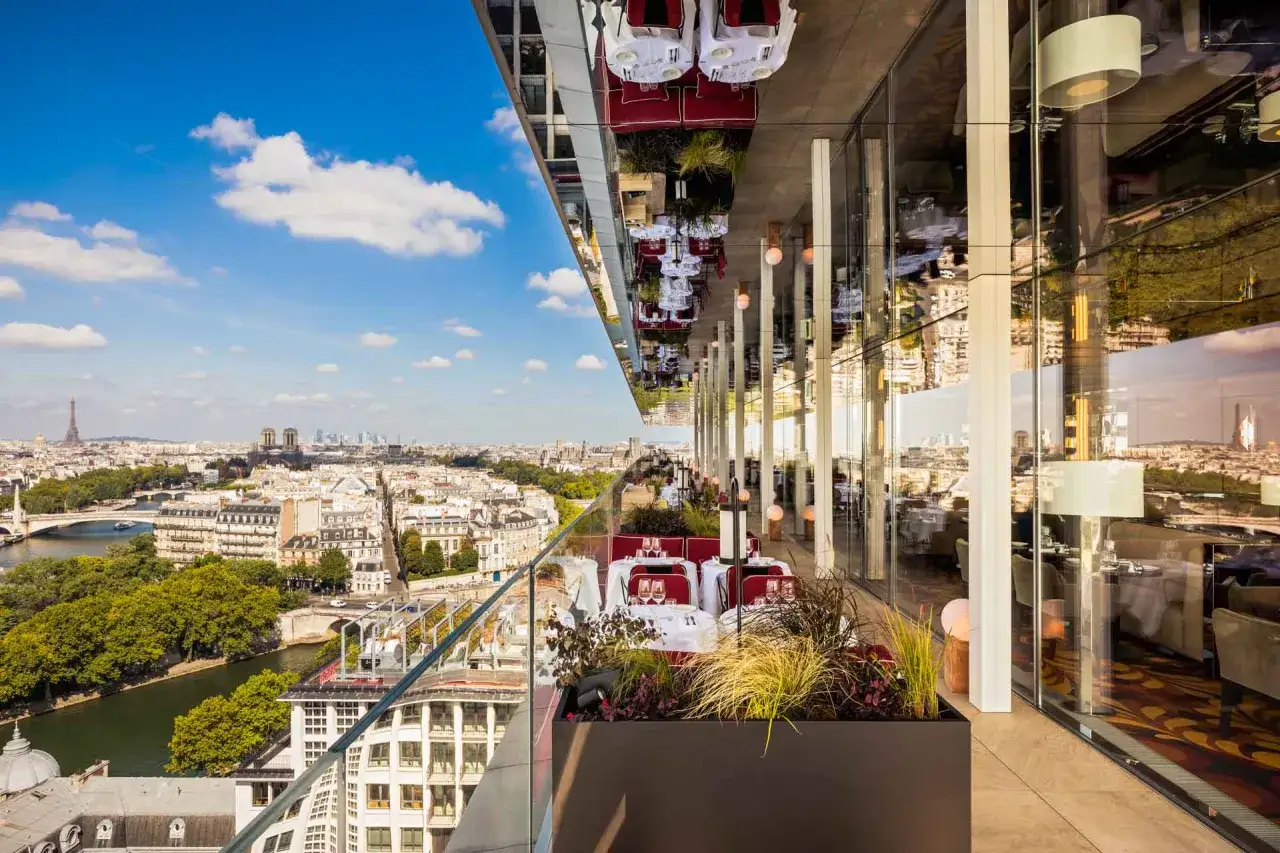 Restaurant avec vue sur la Tour Eiffel. Tables dressées sur une terrasse panoramique, reflets de Paris dans le plafond.