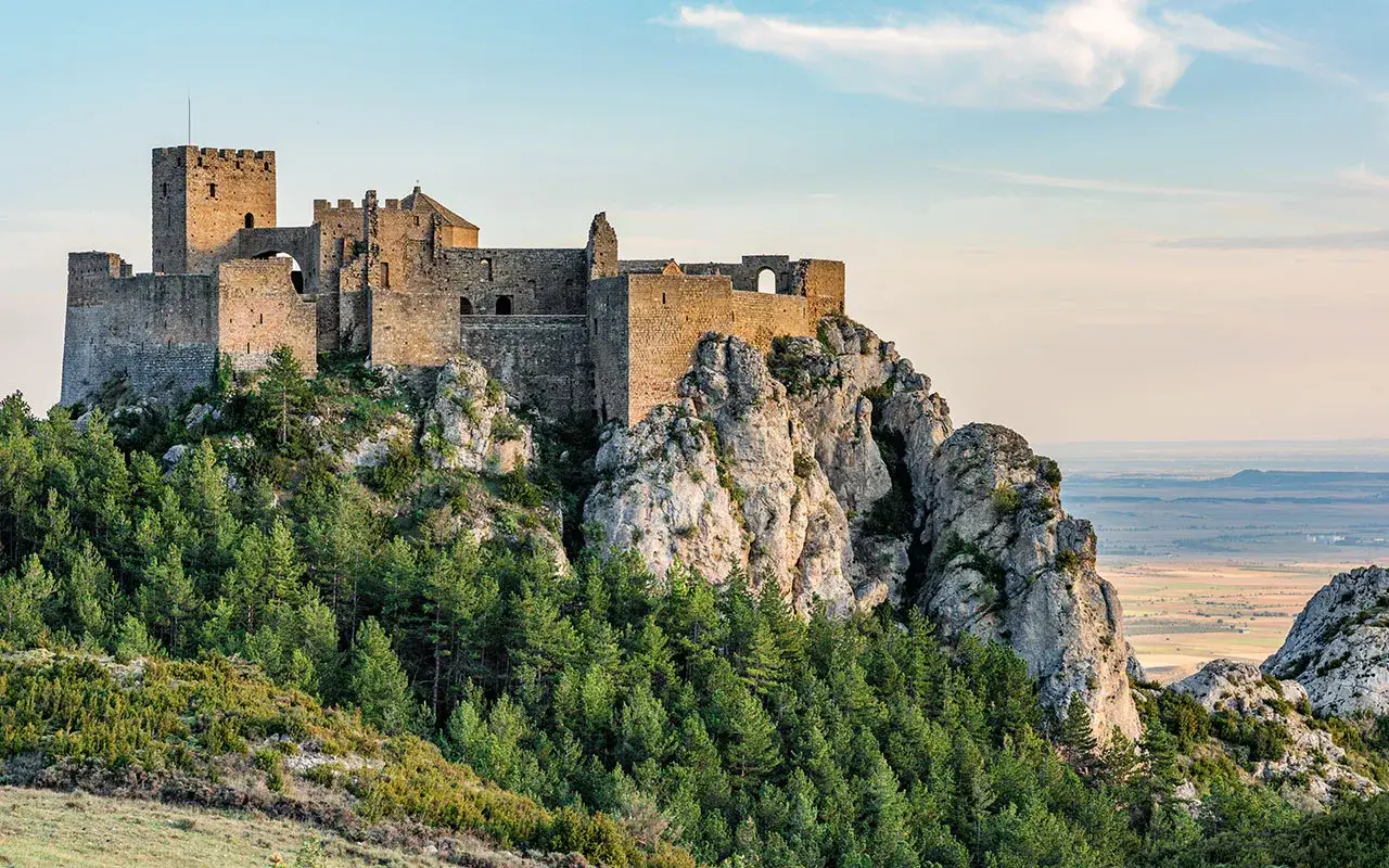 Castillo de Loarre, un lugar imprescindible que ver en Huesca, se alza majestuoso sobre un peñasco rocoso, rodeado de pinos y con vistas a un extenso paisaje.