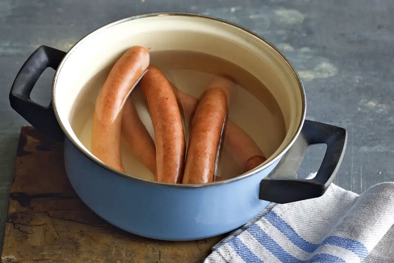 Mehrere Würstchen garen in einem blauen Topf mit Wasser. Die Frage, wie lange Wiener kochen, wird hier visuell angedeutet.