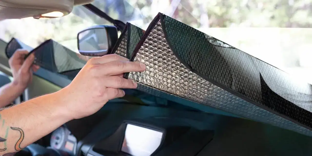 Mani che posizionano un parasole riflettente sul parabrezza per proteggere l'auto dal sole.