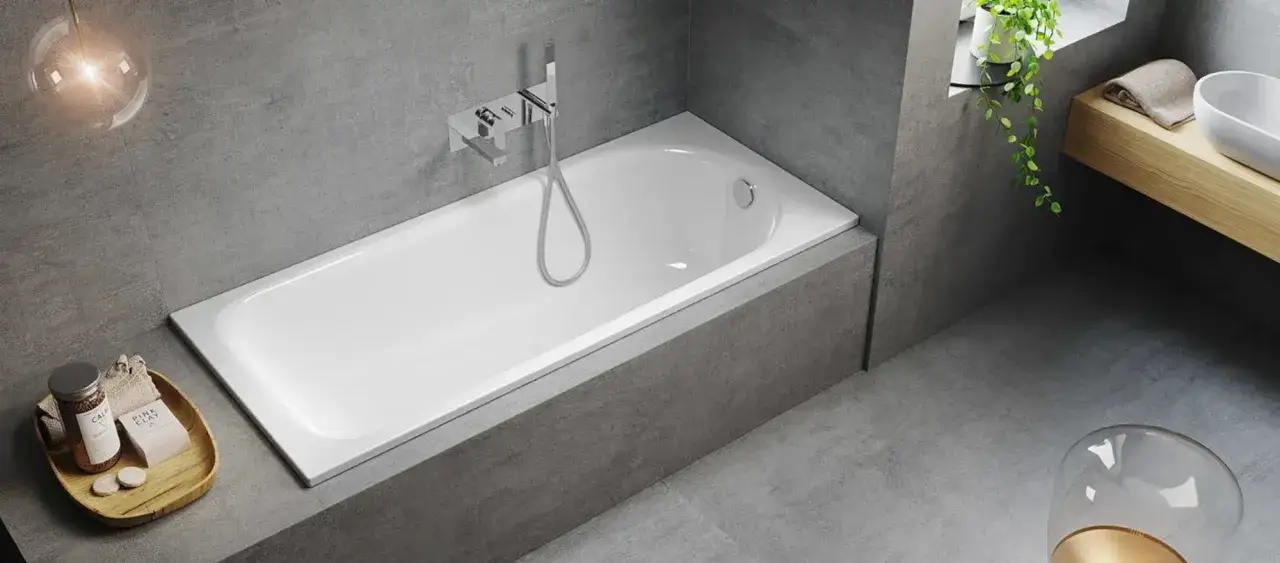 Moderne Badewanne mit Dusche, verkleidet mit grauen Fliesen. Ein Holzelement mit Waschbecken und Pflanzen erg&auml;nzt das stilvolle Ambiente.