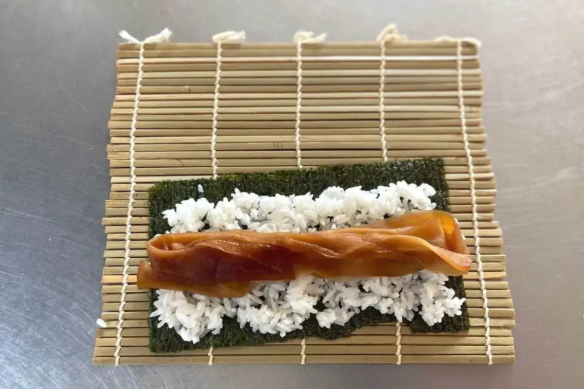 Na macie bambusowej do sushi rozłożono nori, ryż i brązowy, kandyzowany **kanpyo co to** jest, czyli suszoną tykwę.