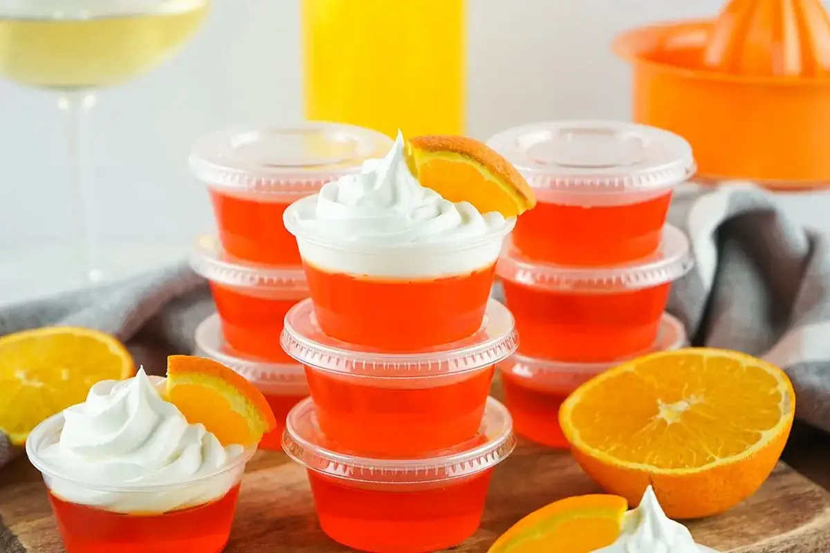 Orange jello shots med vispgr&auml;dde och apelsinskiva. Perfekt f&ouml;r festen!