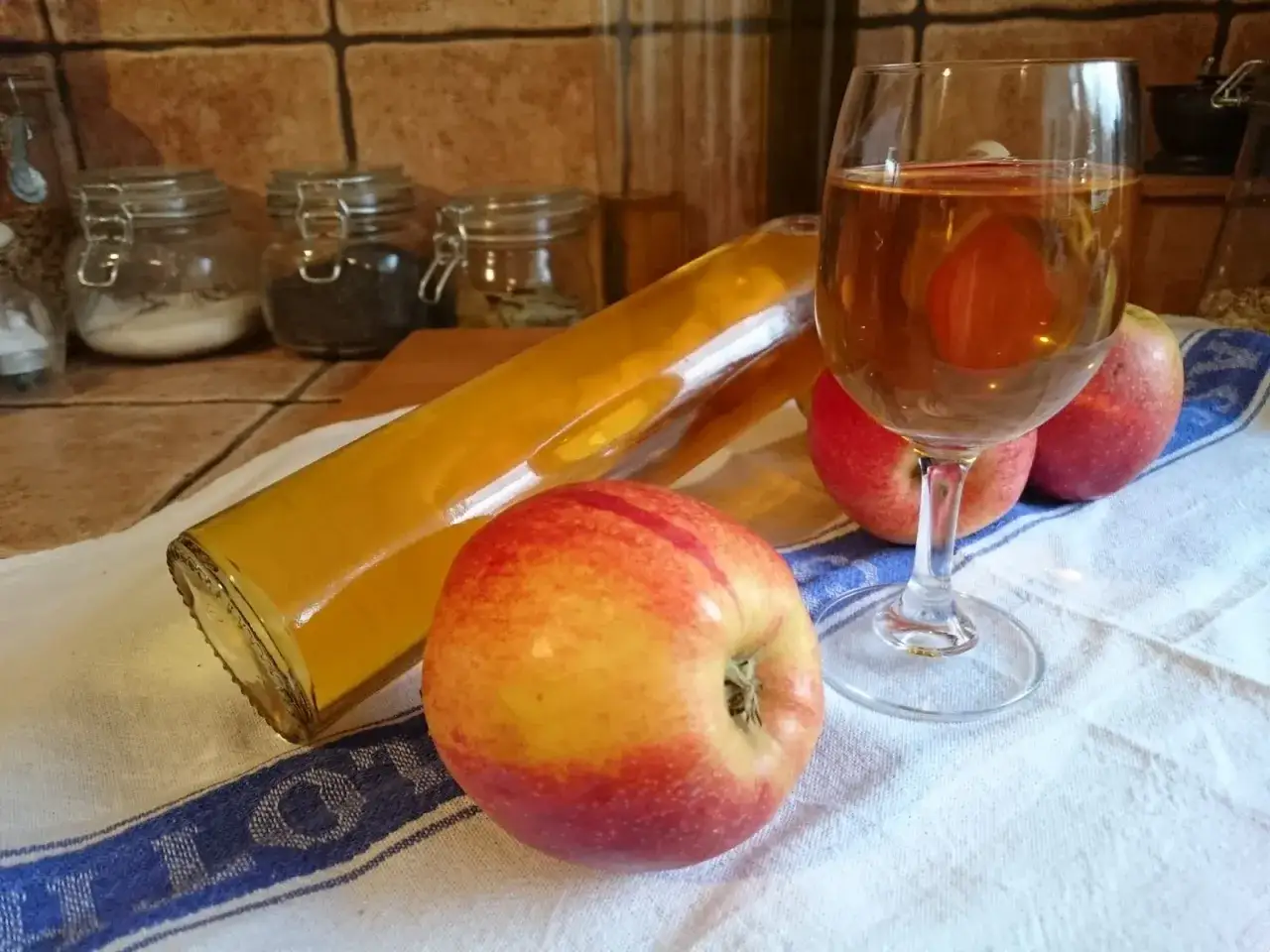 Szklanka i butelka pełne złotego wina z jabłek, obok świeże jabłka.