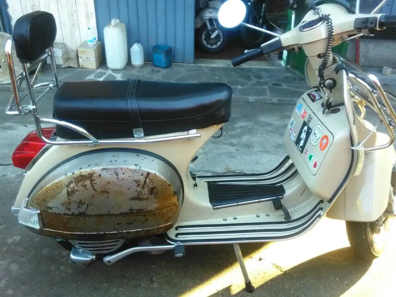 Vespa color crema con sella nera e portapacchi cromato. Il parafango posteriore presenta un evidente **vespa effetto ruggine**, testimone di storie passate.