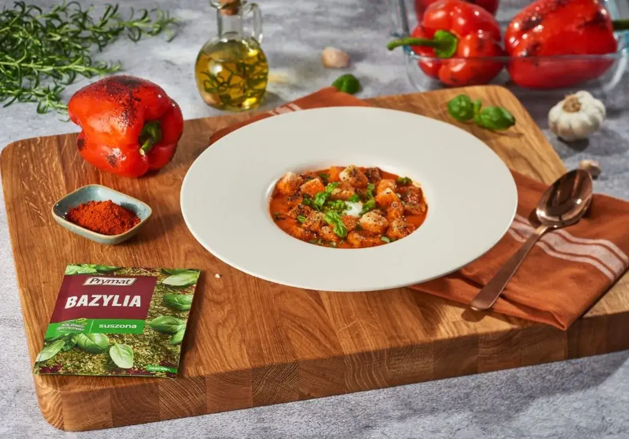 Aksamitny krem z pieczonej papryki z grzankami i bazylią. Obok składniki: papryka, oliwa, czosnek, przyprawy.