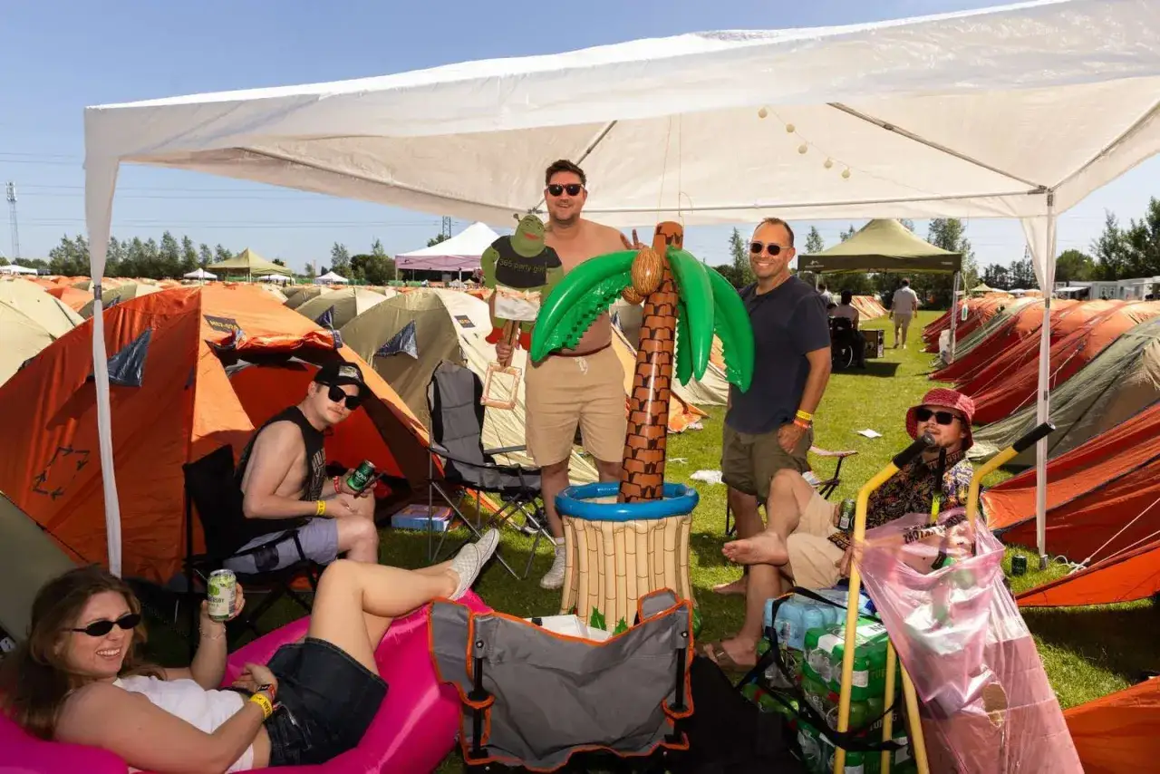 Freunde genie&szlig;en das Roskilde Festival unter Zelten, mit aufblasbarer Palme und Shrek-Figur.