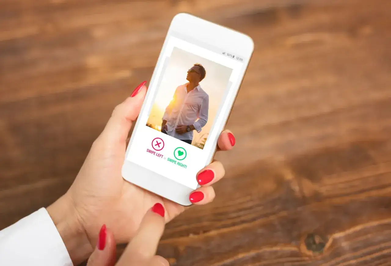 Dłoń z czerwonymi paznokciami trzyma smartfon z profilem na ekranie. Czy to Tinder?