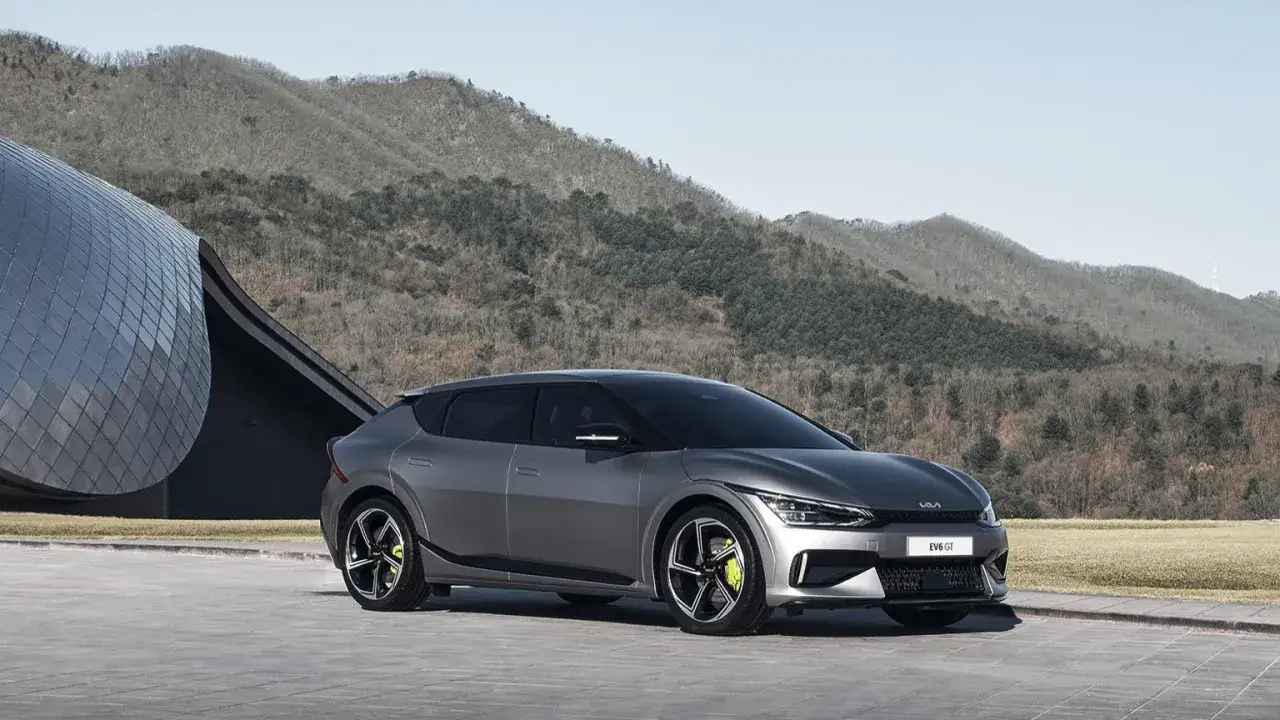 Szary Kia EV6 GT, gotowy do sprintu 0-100 km/h, zaparkowany przed nowoczesnym budynkiem na tle gór.