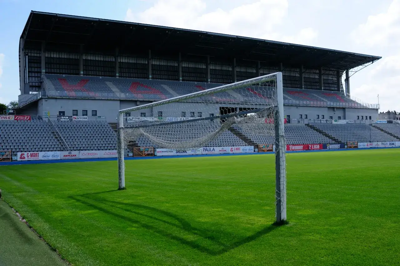 Brama na boisku stadionu KKS Kalisz. Pusta trybuna z czerwonymi siedzeniami w tle.