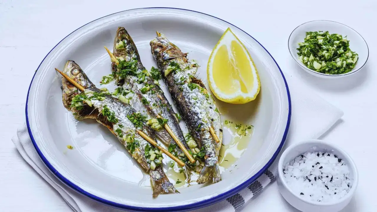 Tres sardinas a la plancha, con ajo y perejil picados, servidas en un plato con limón y sal.