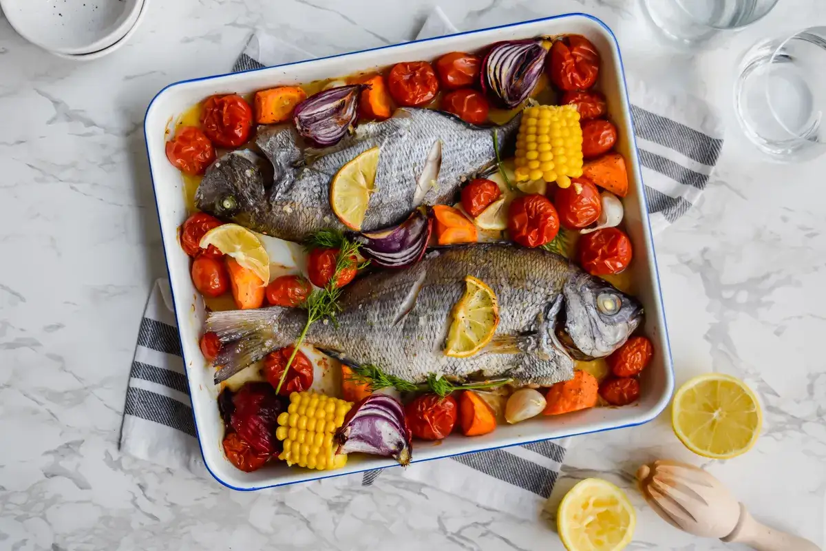Zwei ganze Doraden im Ofen gebacken mit Tomaten, Zwiebeln, Mais und Karotten. Ein leichter Salat w&auml;re hier ideal, um zu fragen: welcher Salat passt zu Dorade?