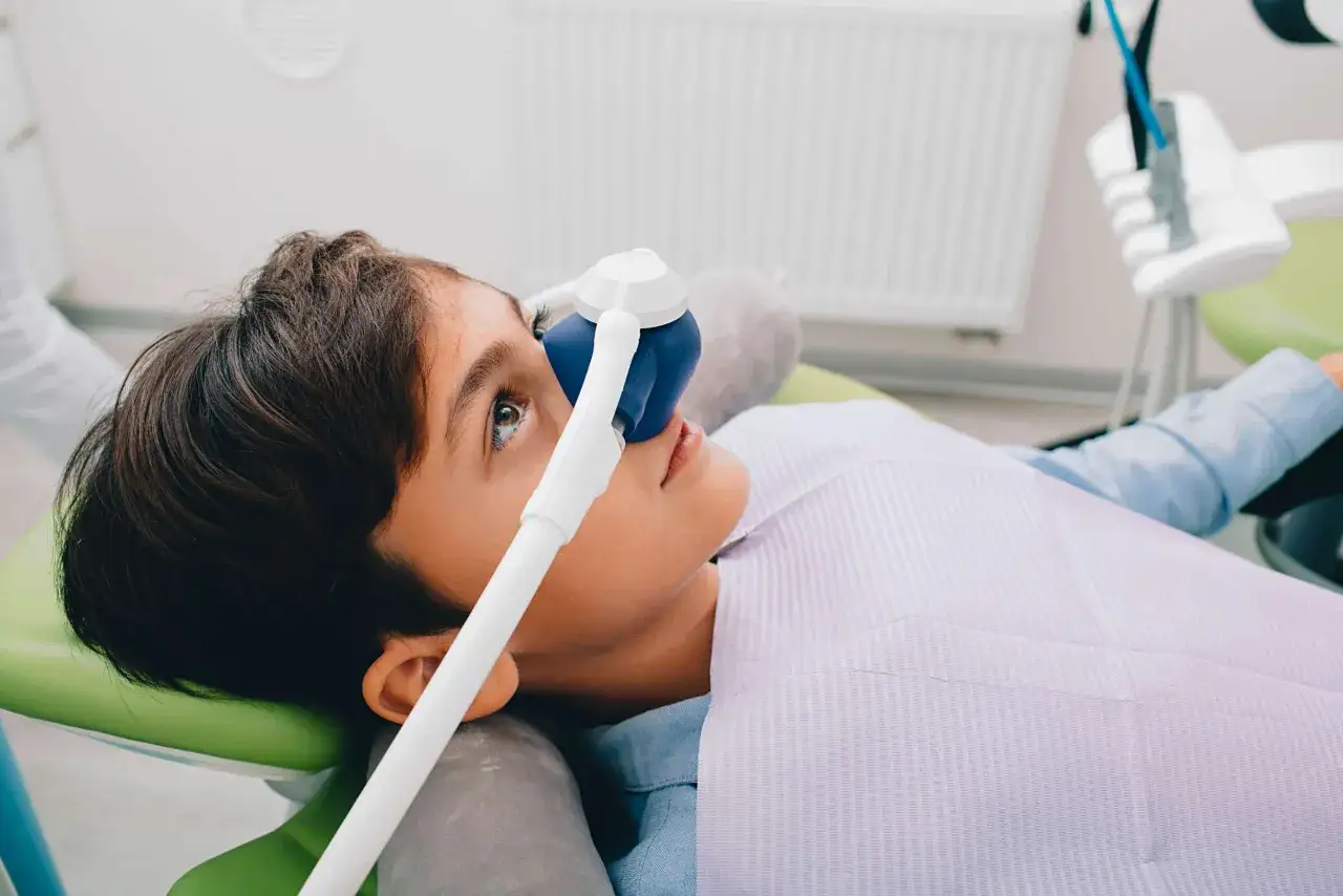 Chłopiec z maską do podtlenku azotu na twarzy, przygotowany na wizytę u dentysty. Gaz rozweselający u dentysty pomaga zredukować stres.