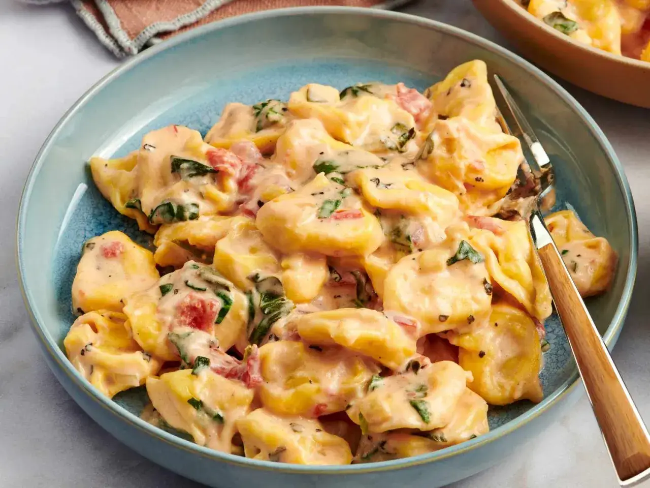 Krämig tortellini med tomater och spenat i en blå skål. Ett perfekt tortellini recept för en snabb middag.