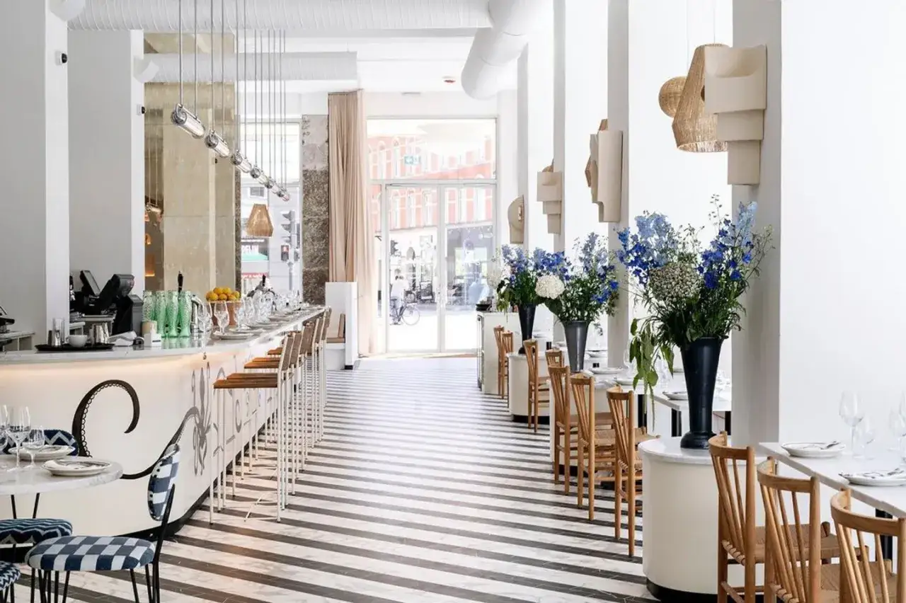 Intérieur lumineux d'un restaurant chic avec un long bar, des tables dressées et des bouquets de fleurs bleues. Un aperçu des meilleurs restaurants Copenhague.