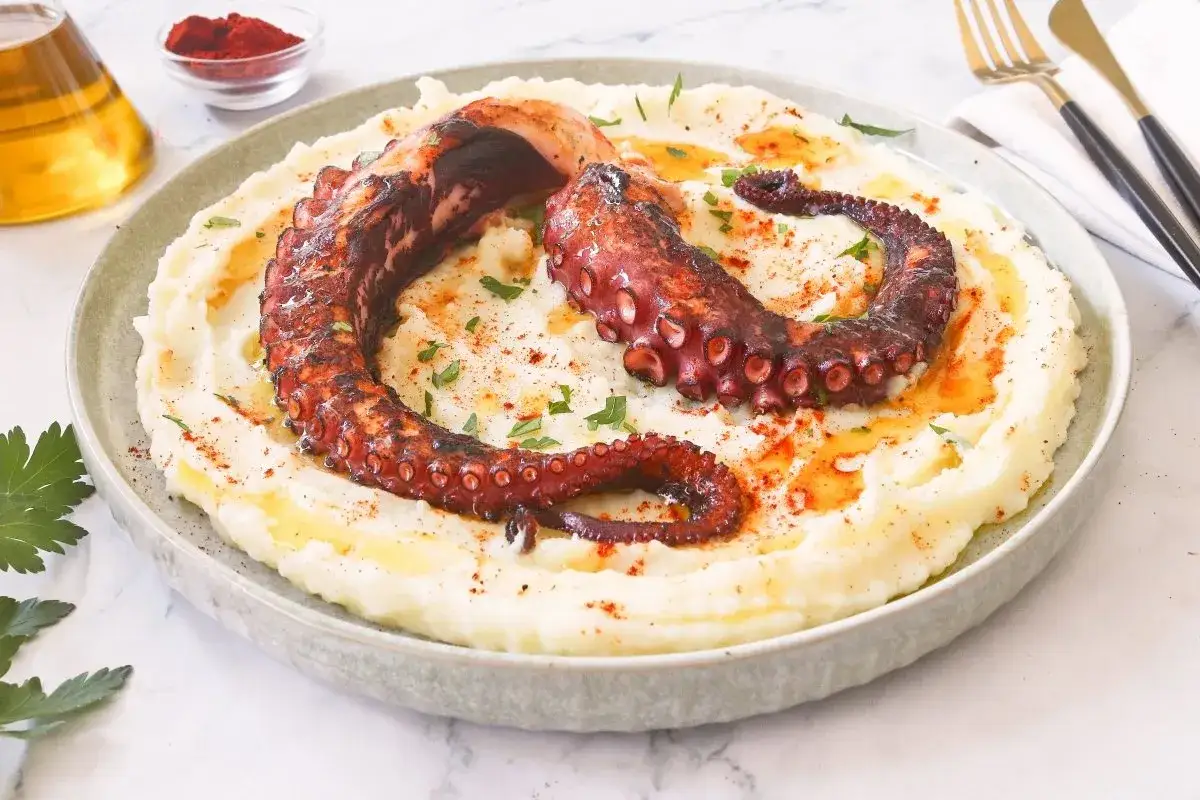 Delicioso pulpo a la brasa sobre pur&eacute; de patatas cremoso, espolvoreado con piment&oacute;n y perejil.