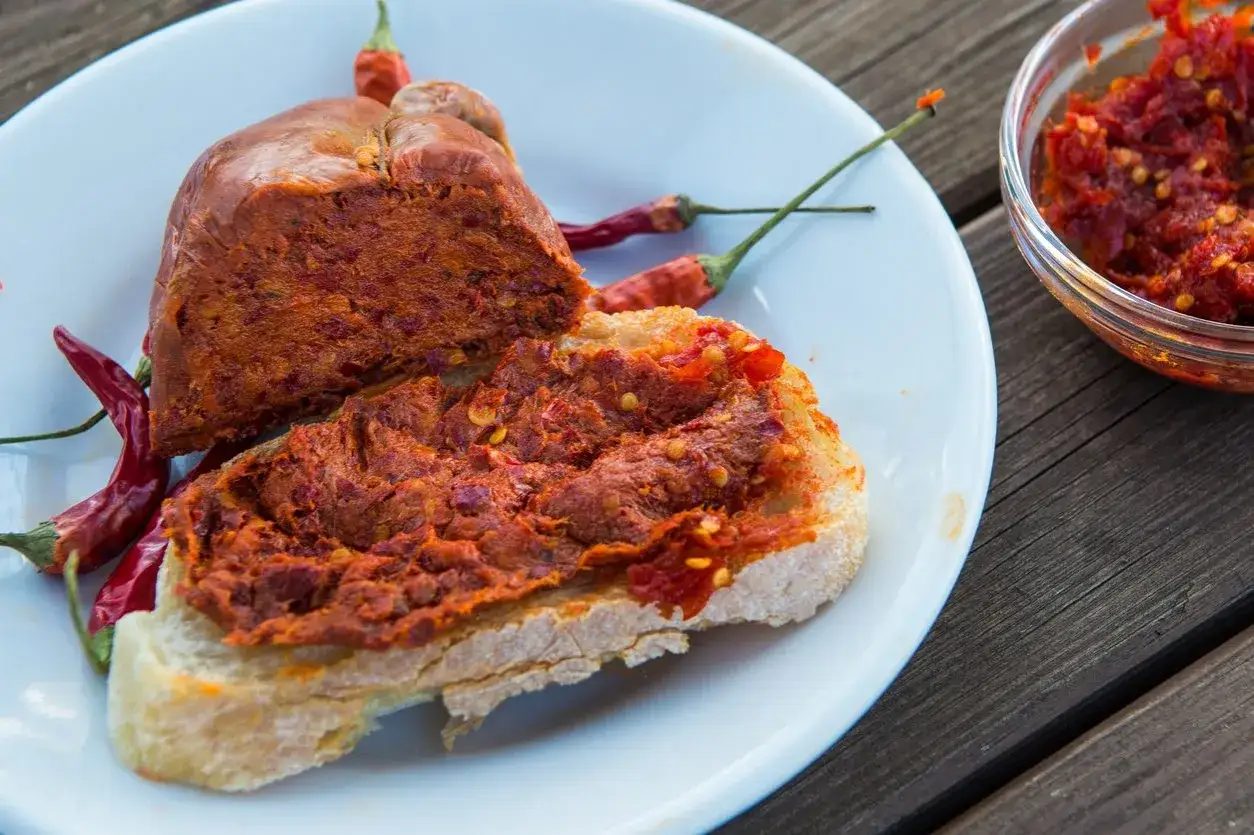 Fetta di pane con 'nduja, un saporito cibo tipico calabrese, accompagnata da peperoncini rossi.