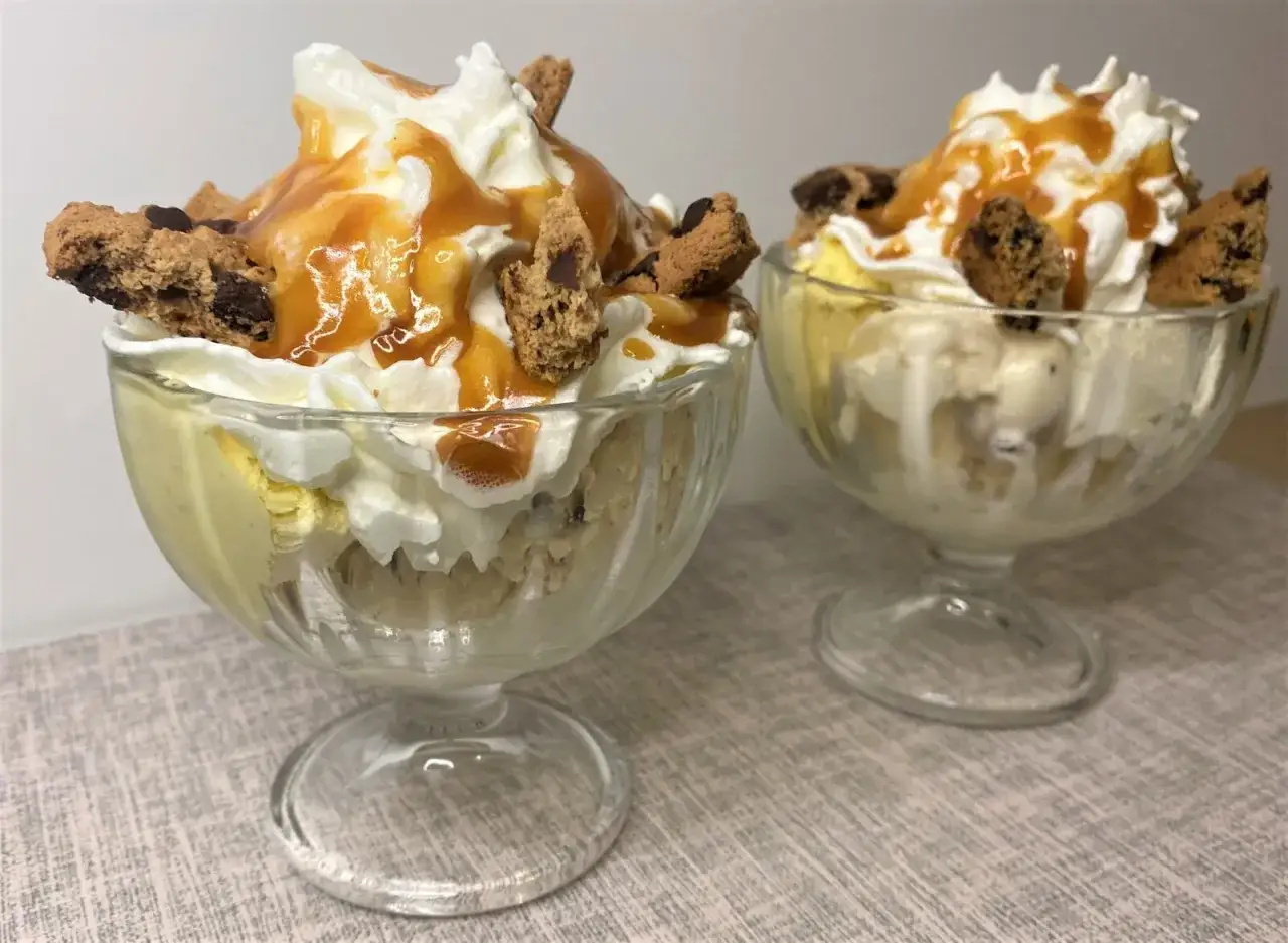 Deux coupes de parfait glacé garnies de crème fouettée, de sauce caramel et de morceaux de biscuits.