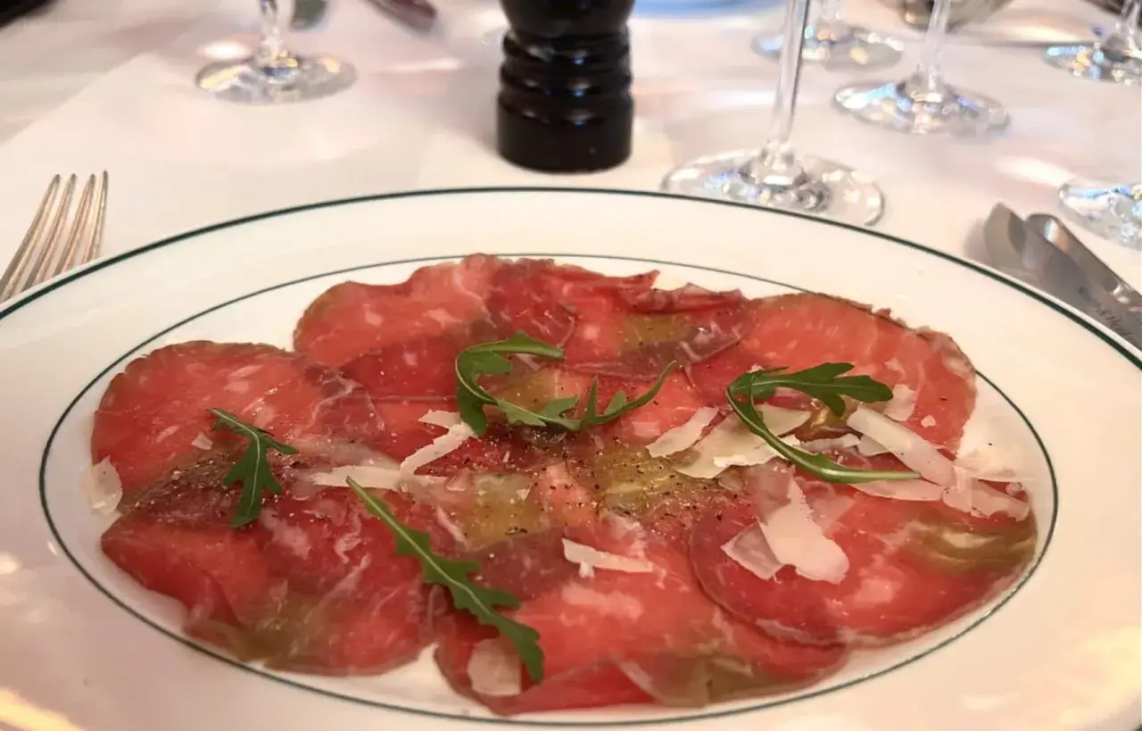 En tallrik med tunnskivad råbiff, toppad med ruccola och parmesan. Perfekt för en förrätt med ett glas vin till carpaccio.