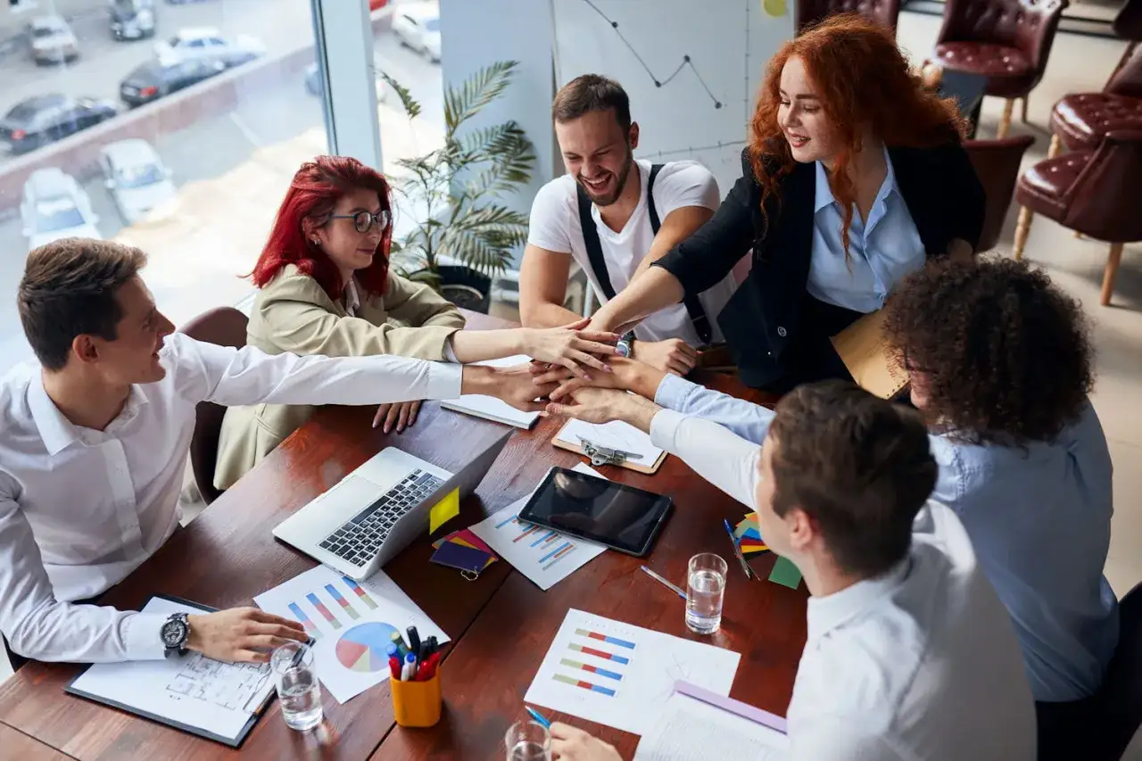 Une équipe soudée applique une technique de management collaborative, mains jointes au-dessus de la table de réunion.