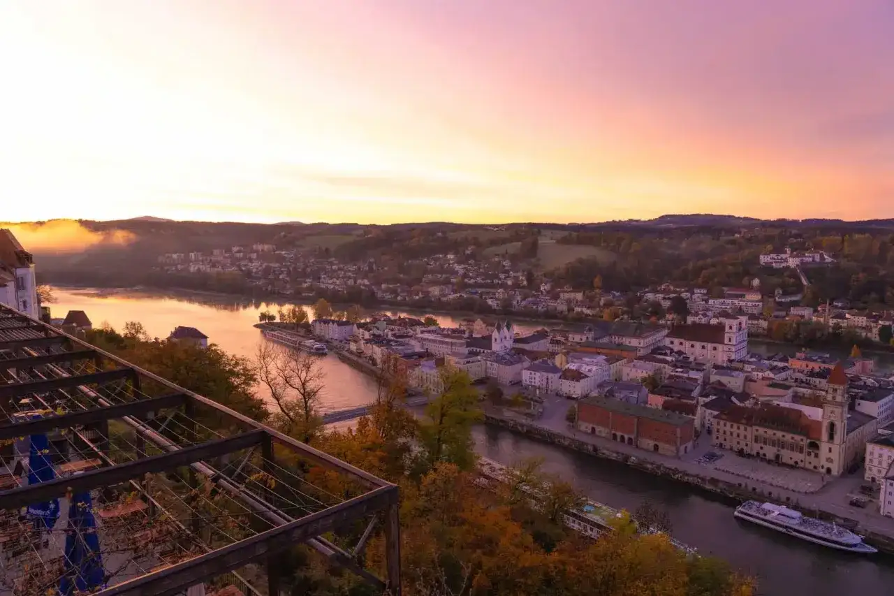Sonnenaufgang &uuml;ber Passau. Die Donau flie&szlig;t durch die Stadt, die von H&uuml;geln umgeben ist. Das Oberhaus Passau thront &uuml;ber der Szenerie.